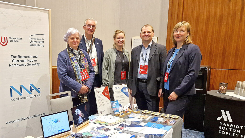 Stand der Universitäten Bremen und Oldenburg mit Informationsmaterialien und Aufstellern, dahinter fünf Vertreter:innen der beiden Universitäten und der U Bremen Research Alliance.