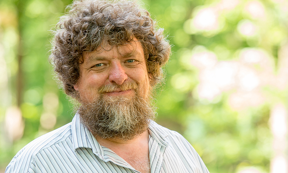 Portraitfoto von Helmut Hillebrand, lächelnd vor einem grünen Hintergrund