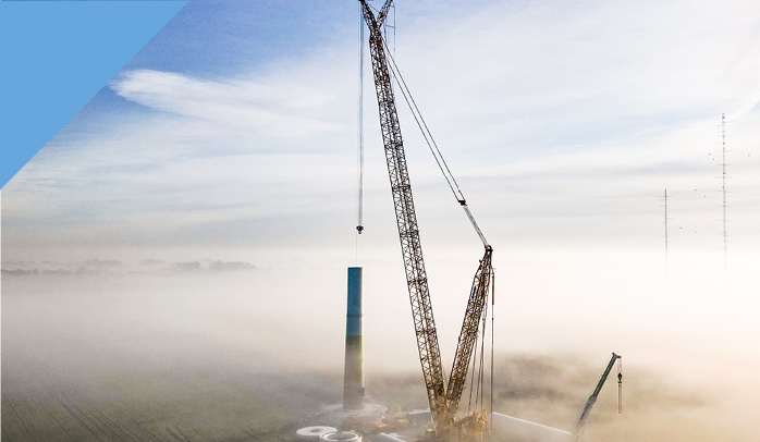 Kräne und Industrieschornsteine in einer Landschaft im Nebel.