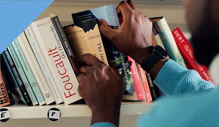 Wissenschaftliche Bücher werden von einer farbigen Person in ein Bücherregal einsortiert.