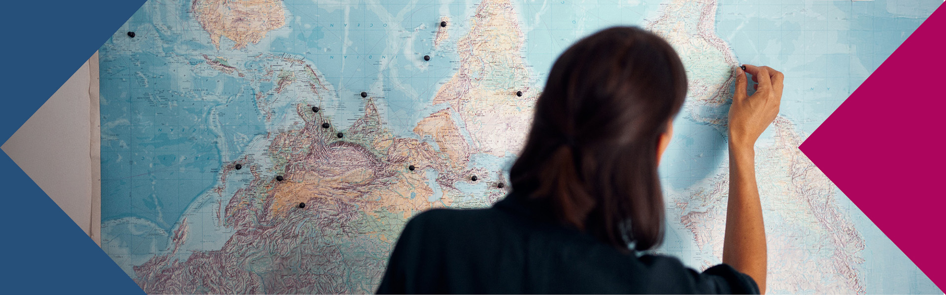 Frau mit schwarzem Pulli pinnt Punkte auf einer Weltkarte an.