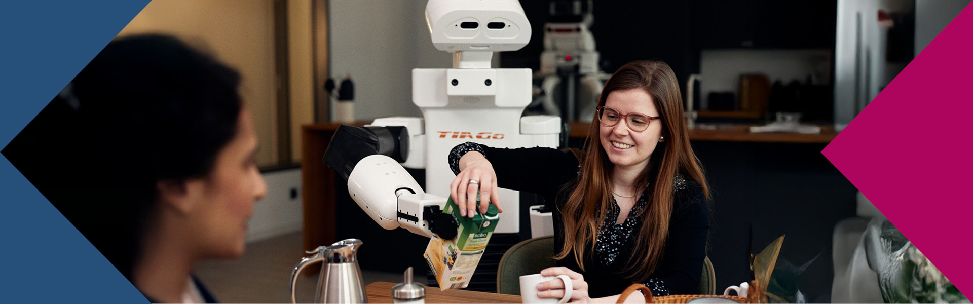 Roboter im Hintergrund unterstützt eine lächelnde jungen Frau beim Einschenken von Milch in eine Tasse.