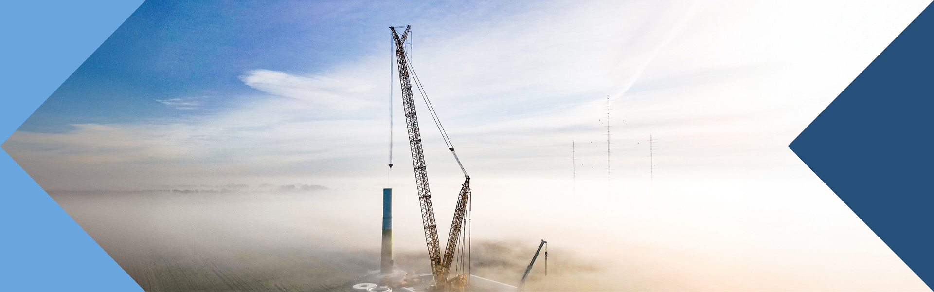 Kräne und Industrieschornsteine in einer Landschaft im Nebel.