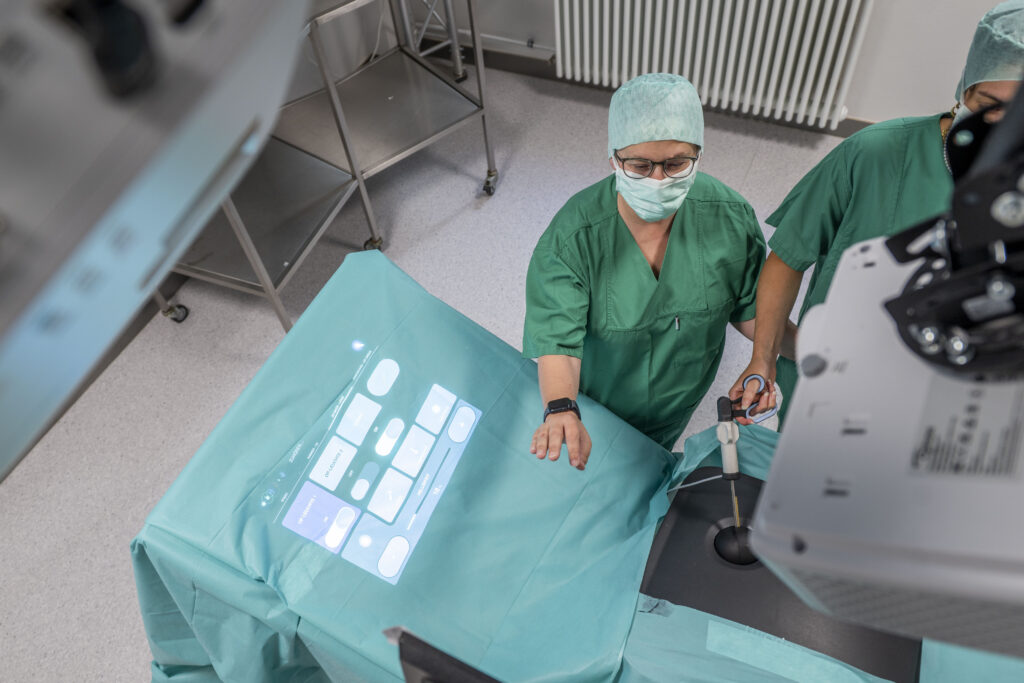 Eine Person steht im OP-Saal, etwas wird auf die Operationsliege projeziert.