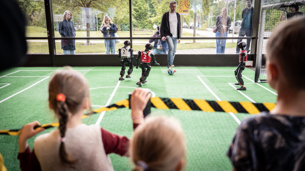 Die Fußballroboter erwiesen sich als wahrer Besucher:innenmagnet und stellten auf dem Spielfeld ihr Können unter Beweis. Ein Mitarbeitender spielt mit den Robotern Fußball.