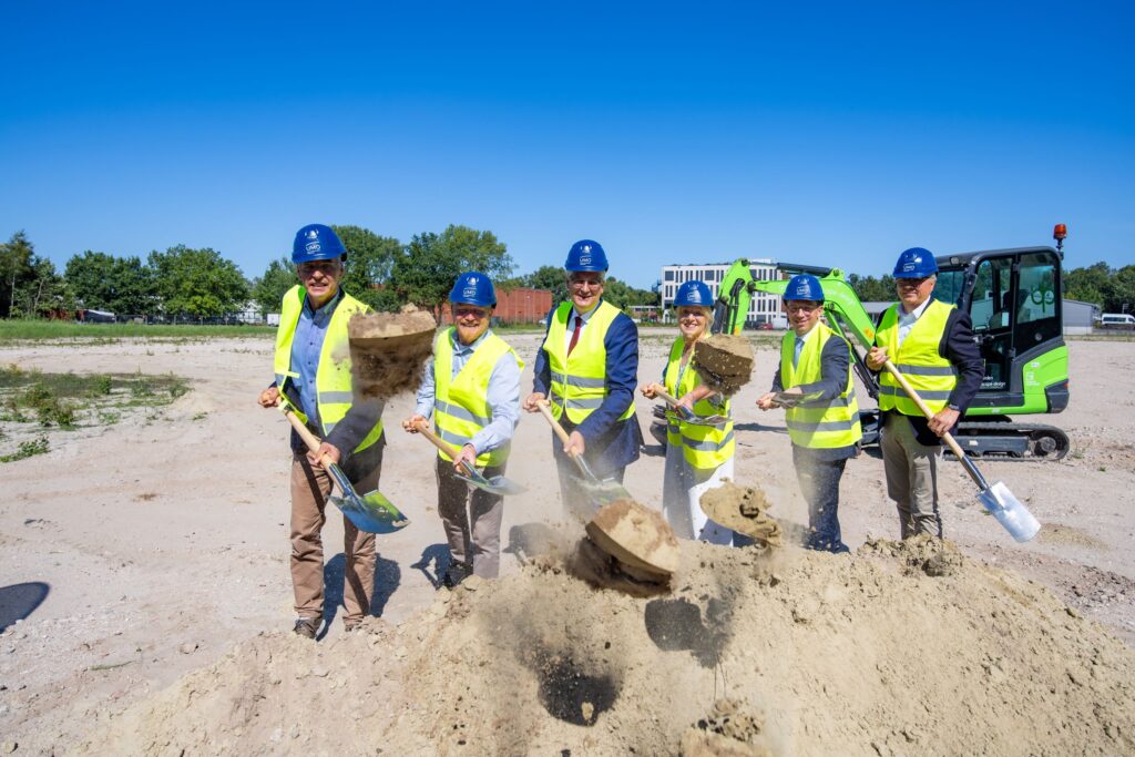 Sechs Menschen stehen mit Schaufeln auf einer Baustelle.