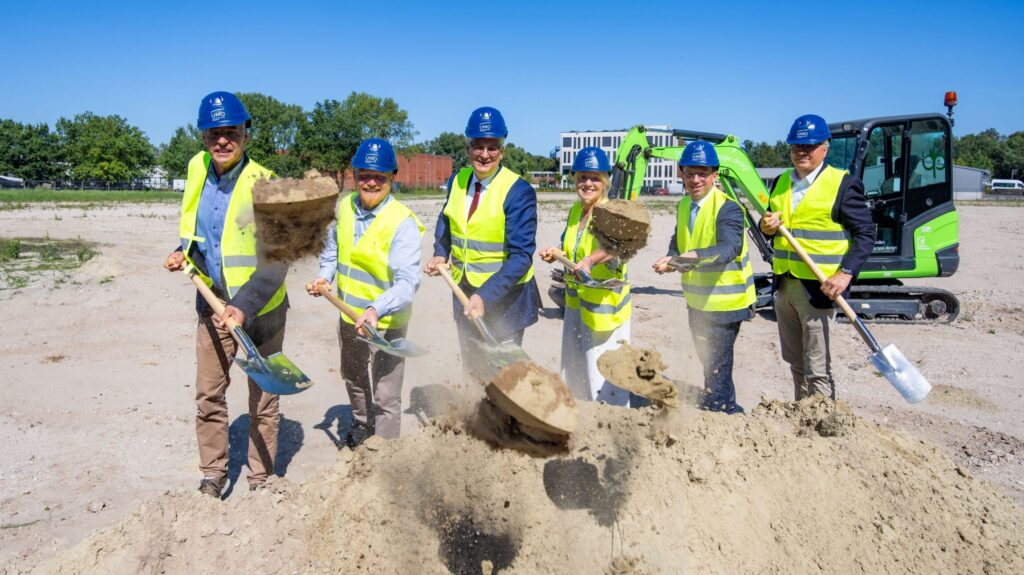 Sechs Menschen stehen mit Schaufeln auf einer Baustelle.